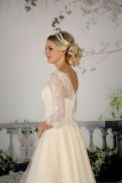 The pretty Cora tea-length bridal gown has a French and corded lace bodice with  illusion neckline and 3/4 length sleeves in champagne